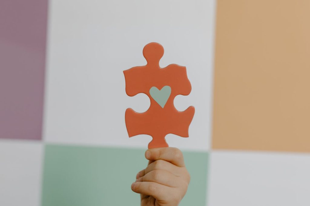 person-holding-orange-puzzle-piece-8386184 A hand holds a red puzzle piece with a heart, symbolizing connection and awareness.